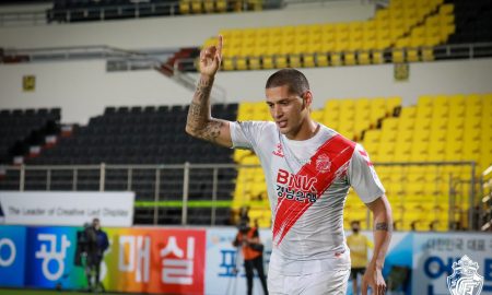 Tiago Orobó está com camisa branca e faixa diagonal vermelha, além de seu braço direito erguido