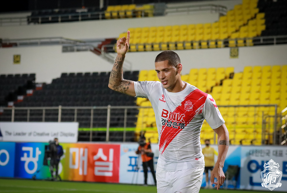 Tiago Orobó está com camisa branca e faixa diagonal vermelha, além de seu braço direito erguido